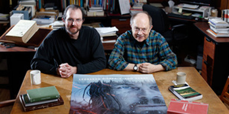 Two men sitting with a Revenant poster