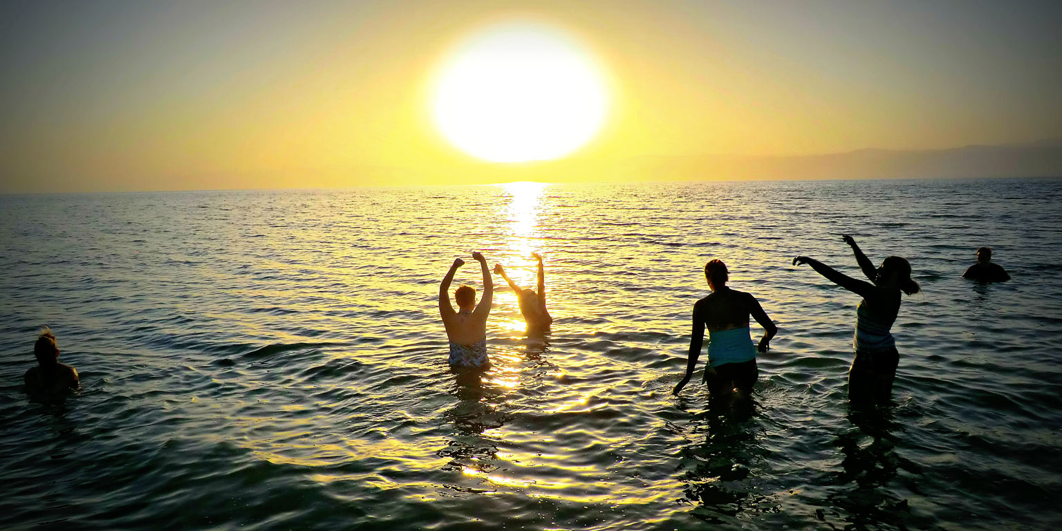People playing in water with a sunset behind them