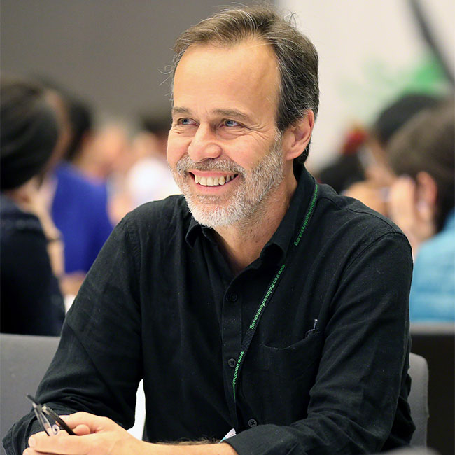 A headshot of Distinguished Professor Eduardo Brondizio, who sits at a table in a black dress shirt.