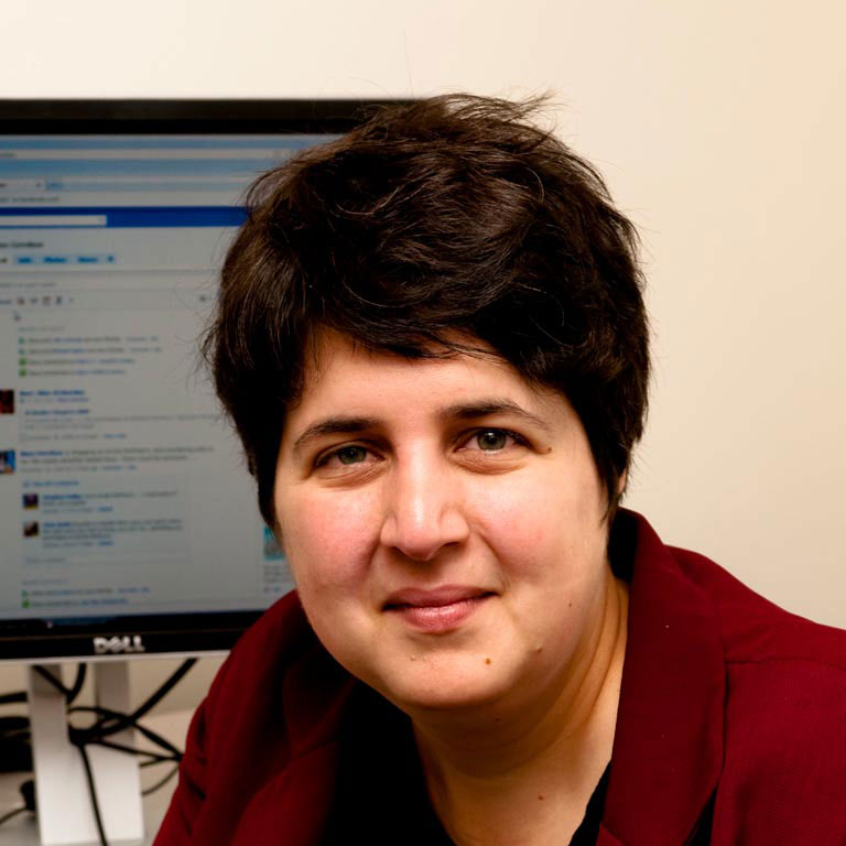 A headshot of Ilana Gershon, who poses in front of a computer screen.