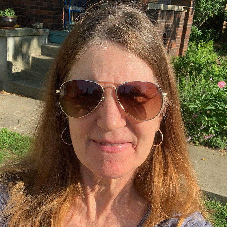 A headshot of Professor Andrea Wiley, who poses outside. She wears sunglasses and a gray shirt.