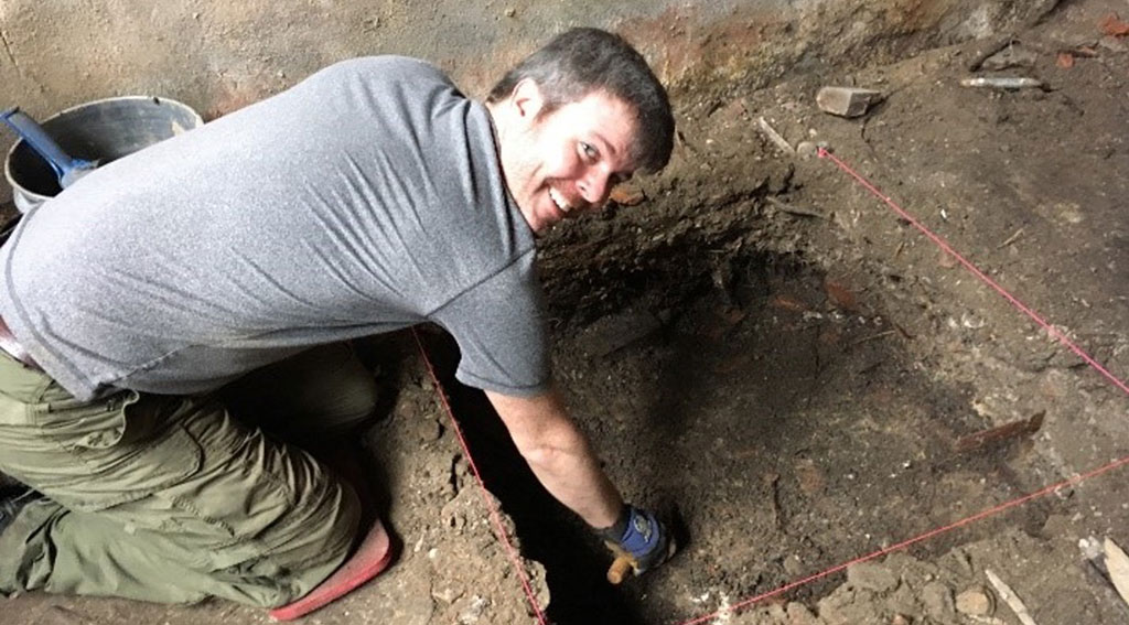 A picture of Ryan Kennedy, who poses while digging at an excavation site.