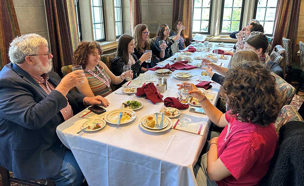 A group of students and faculty members around a table, raising their glasses in a toast.